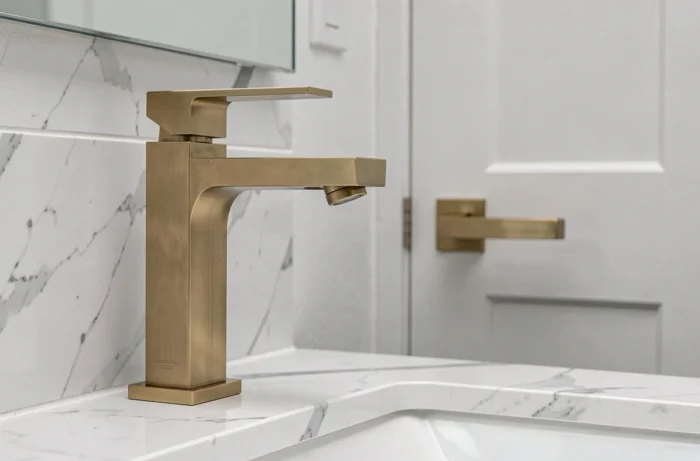 Robinetterie en laiton brossé fraîchement installée sur un plan vasque en marbre blanc avec une poignée de porte assortie visible sur un meuble de salle de bain